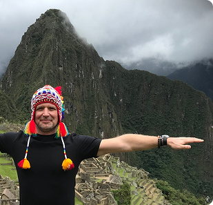 Foto på en man i traditionell mössa som står med armana utåt vid Machu Pichu.