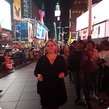 Foto på kvinna som står i en folksamling vid Times Square, kvällstid.