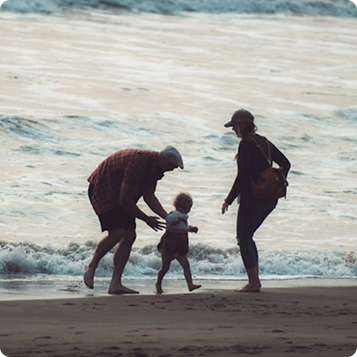 En mamma, pappa och barn går längs strandkanten