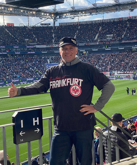 Foto på man med matchtröja som står och ger tummen upp vid en fotbollsmatch.