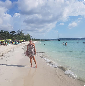Foto på kvinna som står vid strandkanten i ett tropiskt land