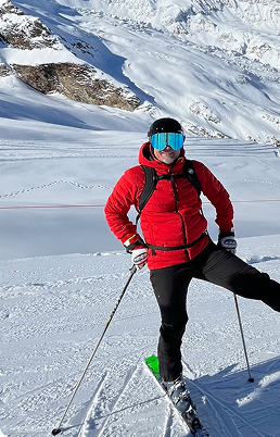 Foto på man i skidutstyrsel som står och poserar i skidbacken.