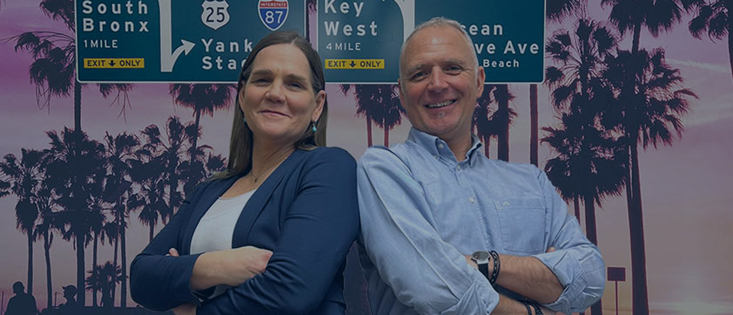 Niklas & cecilia står rygg mot rygg i en bakgrund av amerikanska vägskyltar och solnedgång med palmer.